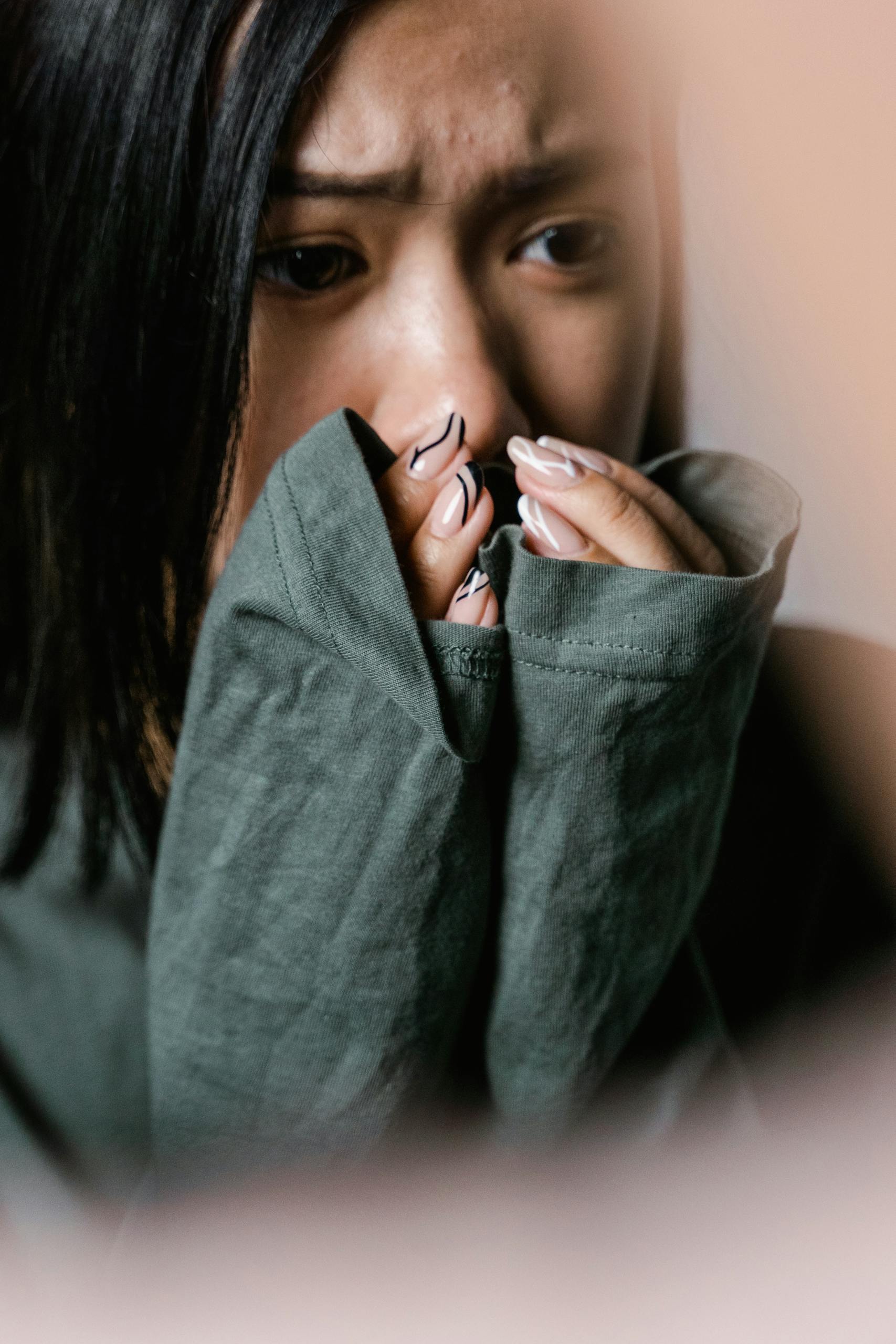 A woman appears anxious, covering her mouth with a green sweater sleeve in a close-up shot.
