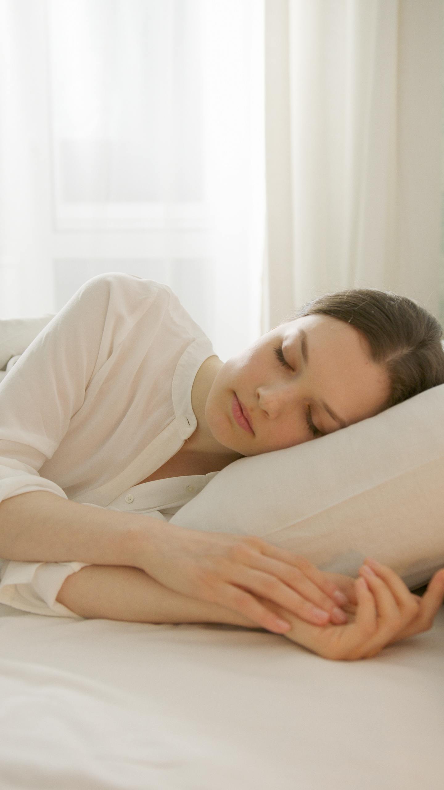 Calm woman sleeping in a white room, reflecting serenity and relaxation, ideal for lifestyle blogs.