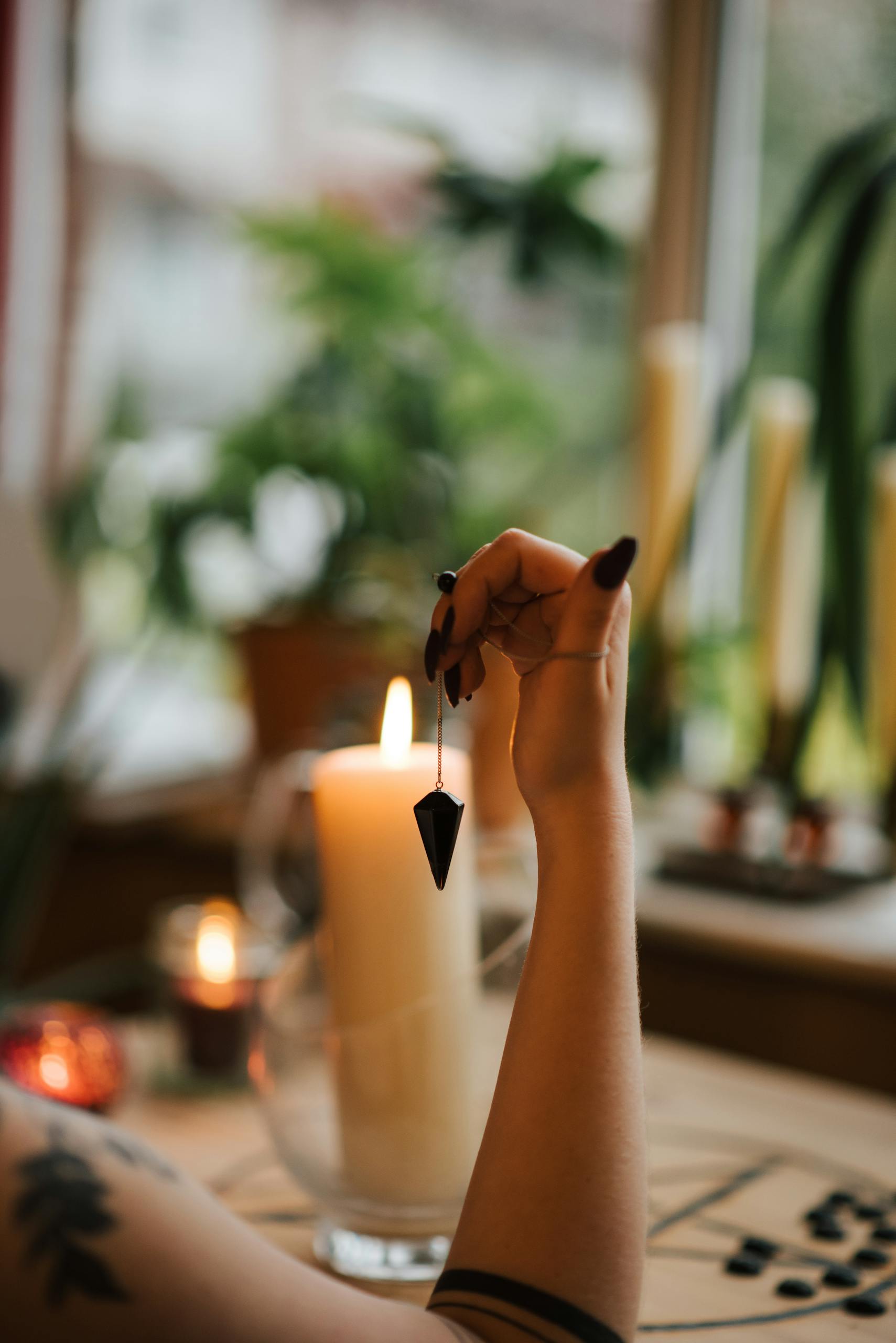 Crop unrecognizable tattooed female soothsayer with talisman near burning candle predicting fate in house