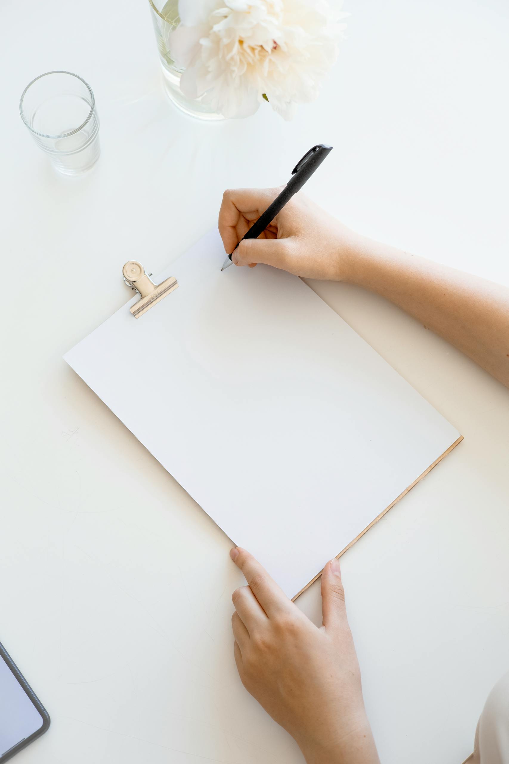 Overhead view of a person writing on a clipboard at a minimalist desk with a flower vase.